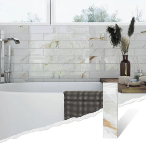 Colamo elongated Calacatta Gold peel and stick subway tile installed as a glossy marble bathroom wall behind a freestanding tub, with a single tile shown in the corner