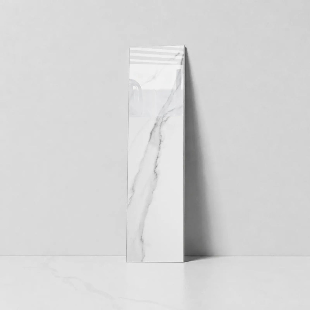 Single Colamo elongated Carrara White peel and stick subway tile with glossy finish and gray marble veining, standing against a light gray wall